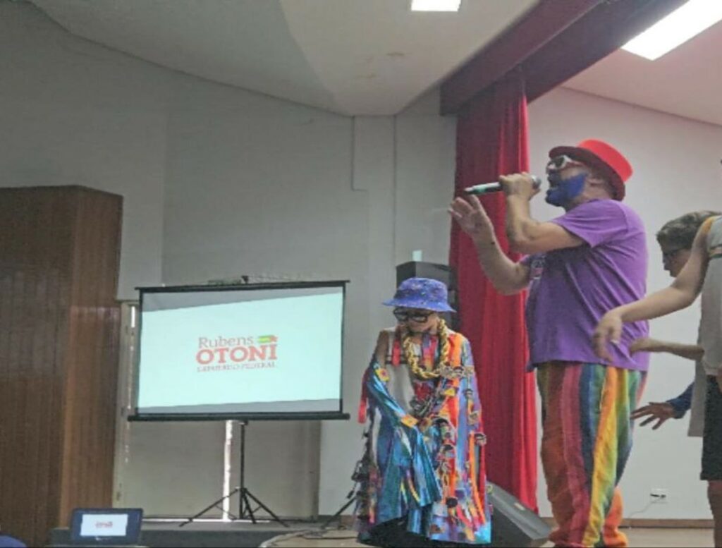 Renan Inquérito no palco do Centro Cultural de Ceres com crianças ao redor enquanto canta com a publicidade do deputado federal por Goiás Rubens Otoni