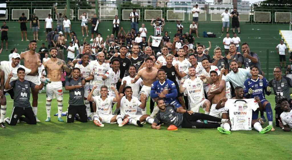 Equipe do Goiânia Esporte Clube reunida para foto oficial após o fim da partida com seus torcedores ao fundo na arquibancada