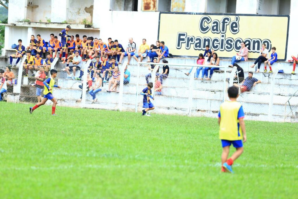 Jogadores em campo com a torcida ao fundo na arquibancada do estádio