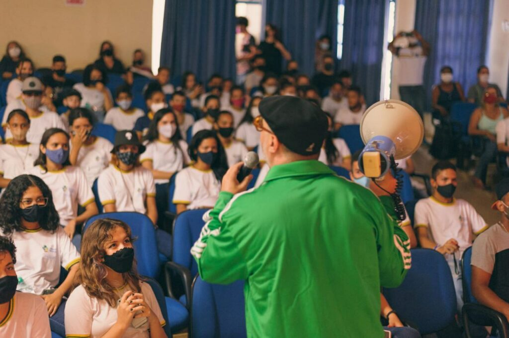 Renan de blusão verde com megafone na mão no palco da UEG de Ceres de frente para alunos do ensino médio