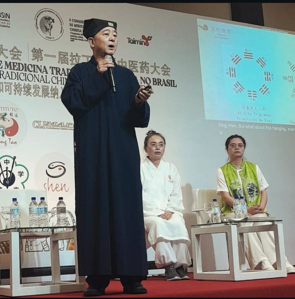 Mestre taóista chinês trajando preto com microfone na mão proferindo sua palestra